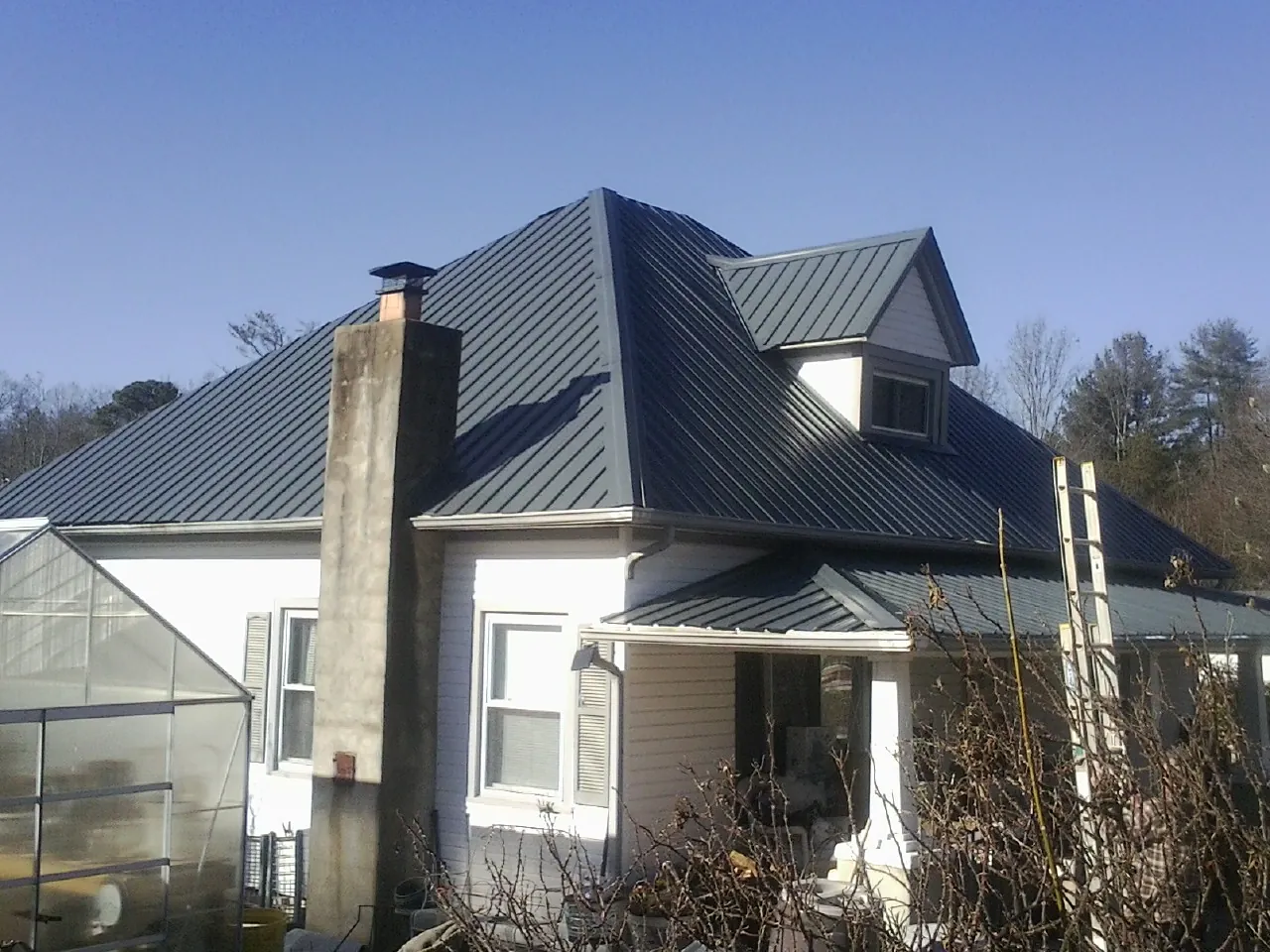 Dark blue standing seam metal roof on a white farmhouse with dormer — Slate & Tile Roof Repair by Roofing Brothers in Ely
