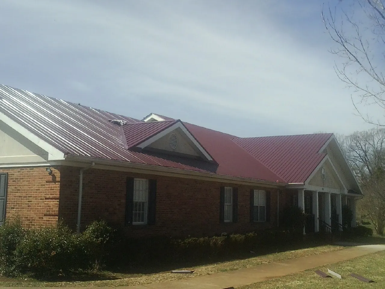 Red metal roof with gabled entries on a long brick building, from a Hail Damage Roof Repair job in Ely