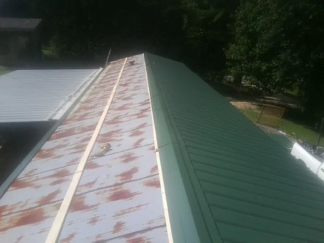 Old rusted panels beside newly installed green metal roofing — Wind Damage Roof Repair by Roofing Brothers in Ely