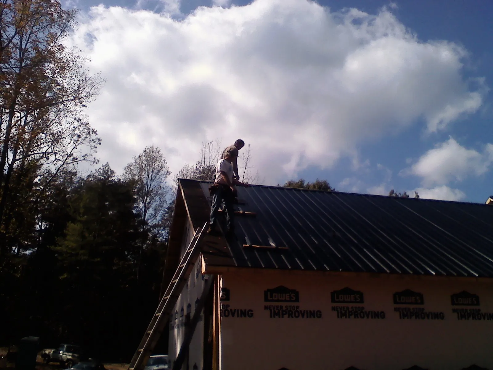 Roofer fastening dark metal panels high against a cloudy sky, from a Roof Inspection job in Ely