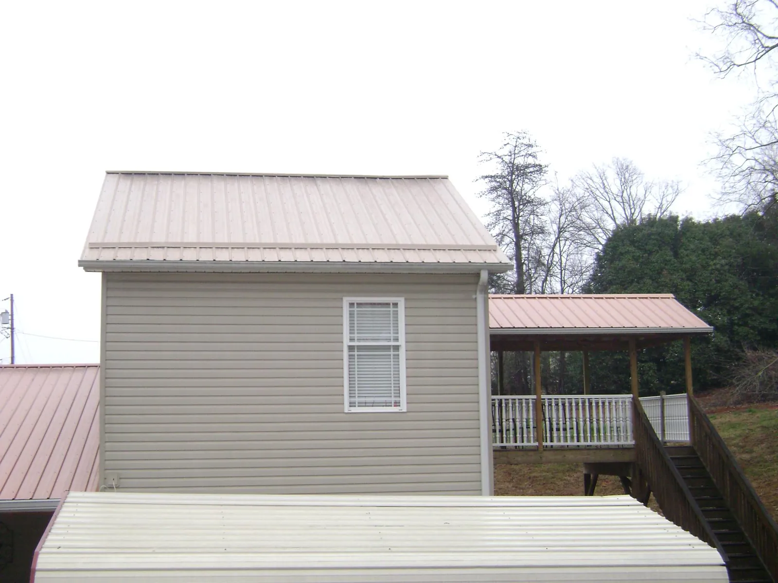 Tan metal roofs on a two story addition and attached porch, from a Roof Replacement job in Ely